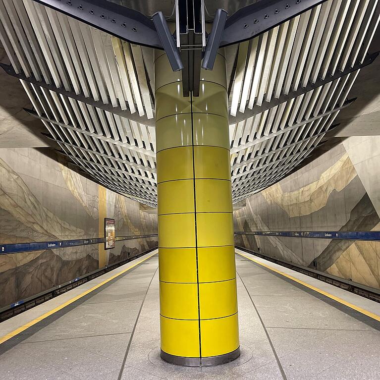 Der U-Bahnhof Gro&szlig;hadern mit gelber S&auml;ule, Wandgem&auml;lde und moderner Lichtabdeckung.