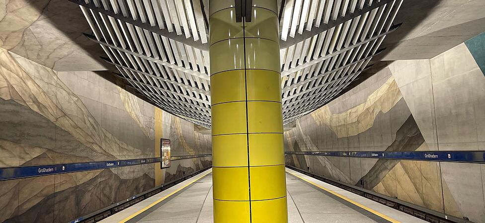 Der U-Bahnhof Gro&szlig;hadern mit gelber S&auml;ule, Wandgem&auml;lde und moderner Lichtabdeckung.
