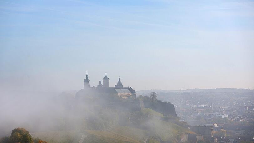Nebel lichtet sich über der von Weinbergen umgebenen Festung Marienberg.