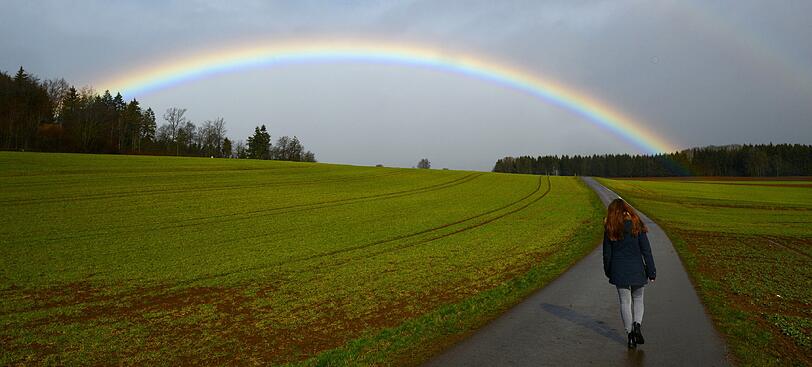 Eine junge Frau läuft am 30.03.2015 bei Behla (Baden-Württemberg) vor einem Regenbogen.