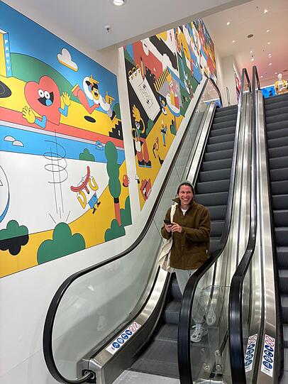 Künstler Sebastian Schwamm fährt gerade die Rolltreppe herunter. Von ihm stammt die Illustration entlang der Rolltreppe. Roter Faden - beziehungsweise blaue Linie - ist darin die Isar.