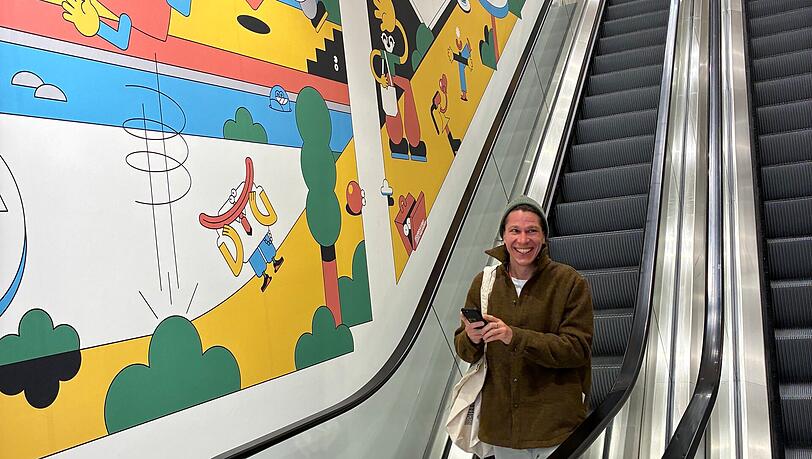 Künstler Sebastian Schwamm fährt gerade die Rolltreppe herunter. Von ihm stammt die Illustration entlang der Rolltreppe. Roter Faden - beziehungsweise blaue Linie - ist darin die Isar. Künstler Sebastian Schwamm fährt gerade die Rolltreppe herunter. Von ihm stammt die Illustration entlang der Rolltreppe. Roter Faden - beziehungsweise blaue Linie - ist darin die Isar.