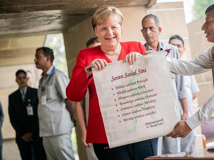 Bundeskanzlerin Angela Merkel bekommt nach einer Gedenkzeremonie für Mahatma Gandhi ein Banner mit den "Seven Social Sins".