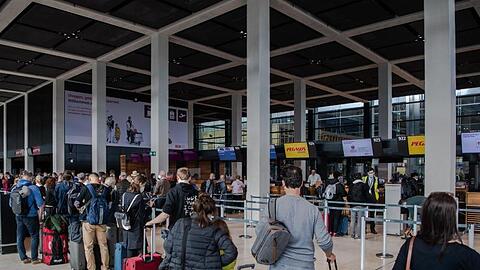 Reisende stehen am Flughafen BER vor einem Check-in-Schalter. Corona-Regeln beschränken weiterhin das freie Reisen.