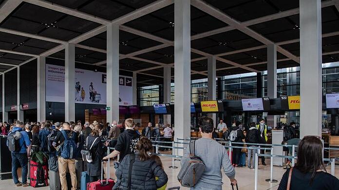 Reisende stehen am Flughafen BER vor einem Check-in-Schalter. Corona-Regeln beschränken weiterhin das freie Reisen.