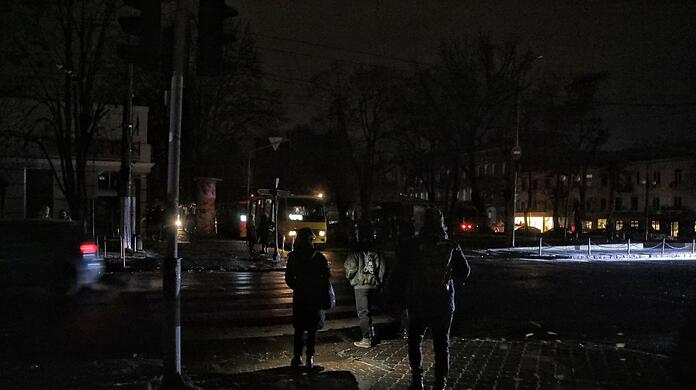 Fußgänger halten sich in Odessa an einer Kreuzung auf einer dunklen Straße auf, da die Stadt von Stromausfällen betroffen ist.