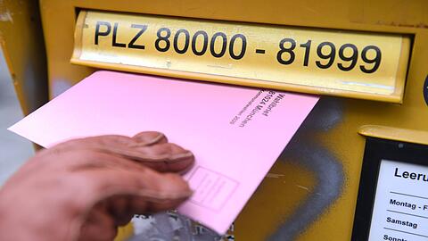 Eine Frau hält die Briefwahlunterlagen für die Kommunalwahl 2020 in der Hand, um diese in einen Briefkasten einzuwerfen.