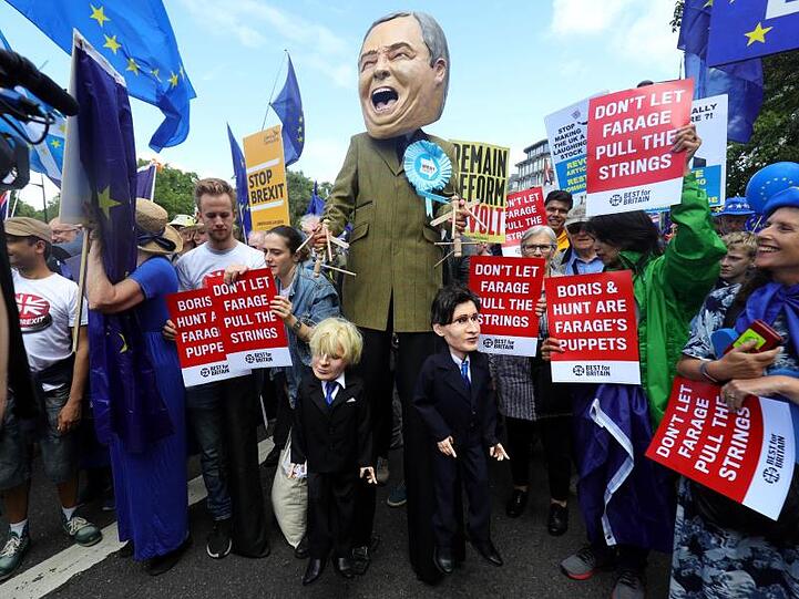 Ein Demonstrant (M) hat sich für den Protestzug als Nigel Farage, Vorsitzender der Brexit-Partei, verkleidet - und hält die Schnüre der Marionetten "Boris Johnson" und "Jeremy Hunt" in den Händen.