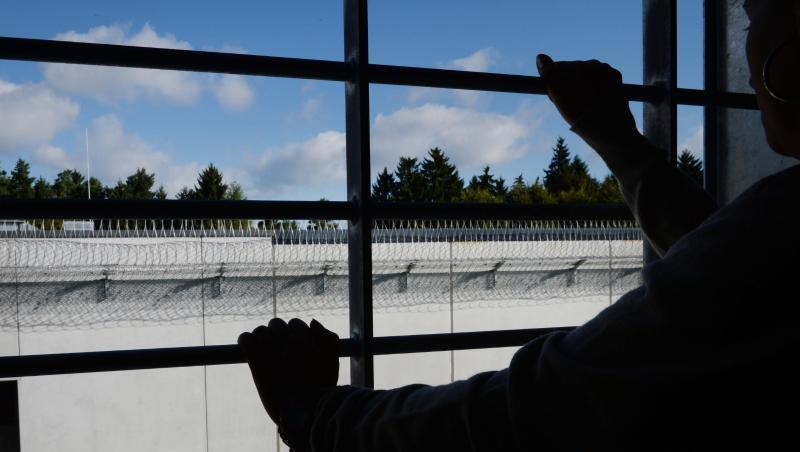 Ein Häftling steht an einem vergitterten Fenster in einer Zelle. Ein Häftling steht an einem vergitterten Fenster in einer Zelle.