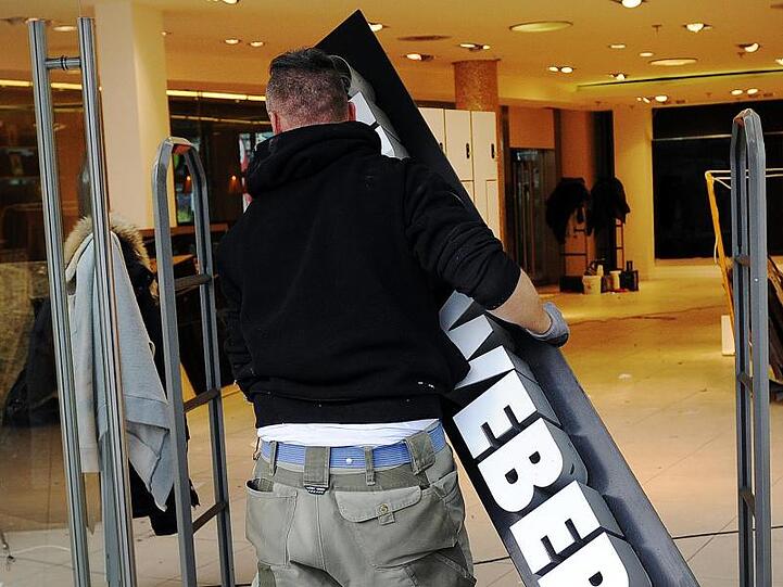 Ein Trockenbau-Monteur hängt ein Schild mit dem Schriftzug "Gerry Weber" an einer geschlossenen Filiale der Modemarke ab.