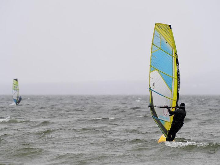 Zwei Windsurfer fahren bei kühlen Temperaturen über den Ammersee. Foto: Felix Hörhager/dpa/Archivbild