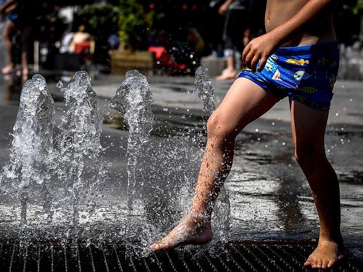 Ein Kind kühlt sich in einem Springbrunnen ab. In Deutschland wird es heiß.