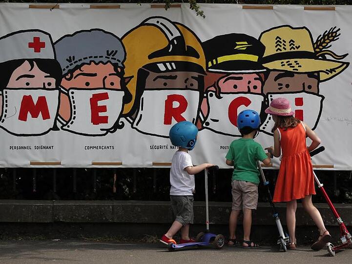Kinder in Paris betrachten ein Banner, auf dem eine Danksagung an verschiedene systemrelevante Berufsgruppen aufgedruckt ist.