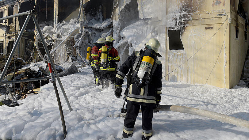 Feuerwehrleute stehen vor ausgebrannten Wohncontainern. Nachts kam es in dieser Asylunterkunft aus unbekannter Ursache zu einem Brand, bei dem drei Bewohner verletzt wurden.