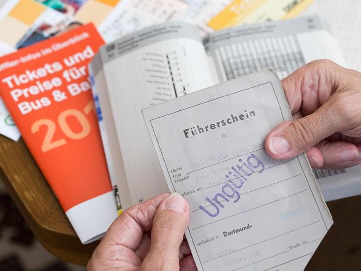 Eine ältere Person hält ihren entwerteten Führerschein in der Hand. Im Hintergrund ist ein Fahrplan des Öffentlichen Personen-Nahverkehrs zu sehen. Foto: Friso Gentsch/Archiv