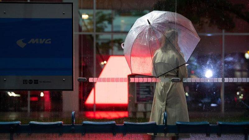 Eine Frau wartet mit ihrem Regenschirm an einer Bushaltestelle auf den Bus.