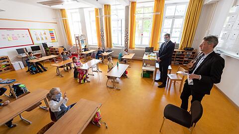 Seit Montag sind auch Erstklässler wieder in der Schule. Zum Start schauen sich an der Kirchenstraße in Haidhausen Kultusminister Michael Piazolo (r., Freie Wähler) und Ministerpräsident Markus Söder (CSU) an, ob die Tische auch weit genug auseinander stehen.