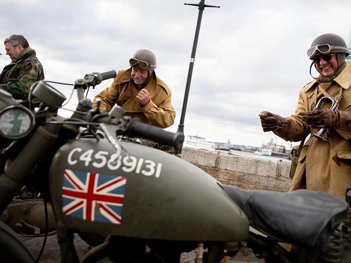 Drei Briten stehen in historischen Uniformen mit historischen Motorrädern in der Altstadt von Portsmouth.