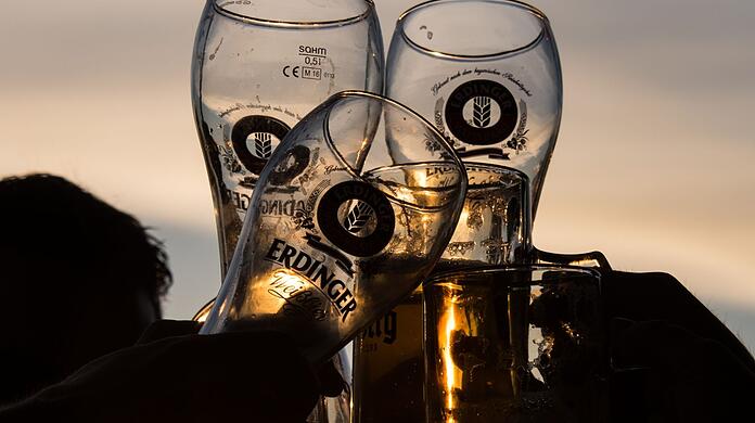 Junge Menschen stoßen im Sonnenuntergang in einem Biergarten mit Biergläsern an.
