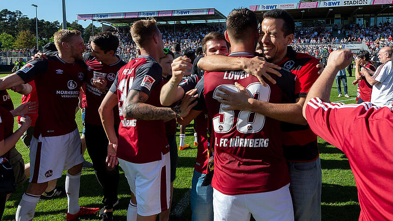 Freude pur: die Spieler des FC Nürnberg liegen sich nach dem geglückten Aufstieg in den Armen, im Hintergrund stürmen die Fans den Platz.