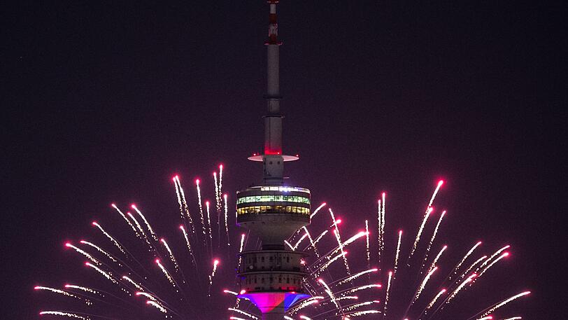 Der Himmel hinter dem Olympiaturm wird durch Feuerwerksraketen hell in einem Rosa-Ton erleuchtet.