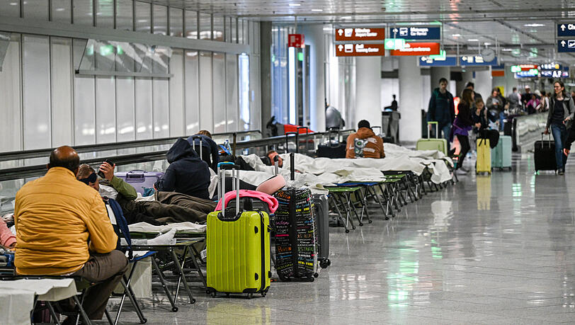 Menschen warten nach Drohnensichtungen und Flugausfällen in Flughafen München auf Feldbetten. Wegen Drohnensichtungen sind am Flughafen in München am Donnerstagabend rund 20 Flüge ausgefallen. Statt wegzufliegen, mussten die Leute die Nacht auf dem Flughafen München verbringen.