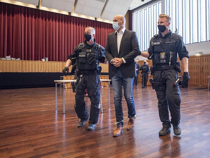 An Händen und Füßen gefesselt ist einer der Hauptangeklagten, den bewaffnete Polizisten in die zu einem Gerichtssaal umfunktionierte Kongresshalle in Gießen bringen.