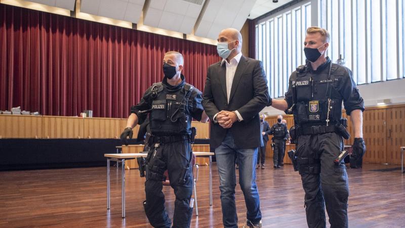 An Händen und Füßen gefesselt ist einer der Hauptangeklagten, den bewaffnete Polizisten in die zu einem Gerichtssaal umfunktionierte Kongresshalle in Gießen bringen.