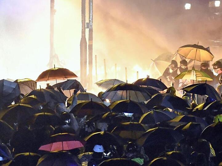 Demonstranten schützen sich mit Regenschirmen auf dem Campus der Polytechnischen Universität in Kowloon vor den Wasserwerfern der Polizei.
