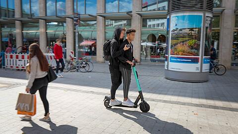 Drei Verstöße auf einem Bild: zu zweit auf dem E-Scooter, Fahrt durch die Fußgängerzone, Mobiltelefon in der Hand.