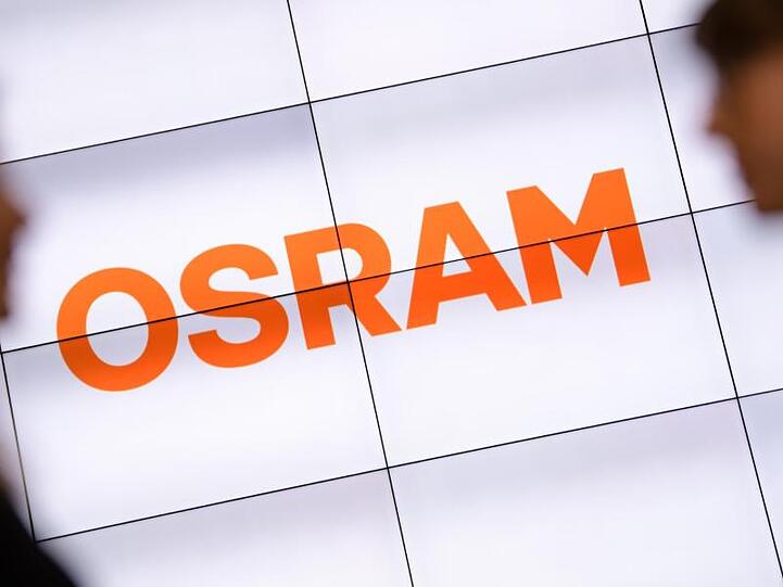 Zwei Frauen unterhalten vor einem über mehrere Monitore dargestellten Osram-Logo. Foto: Matthias Balk/dpa/Archivbild