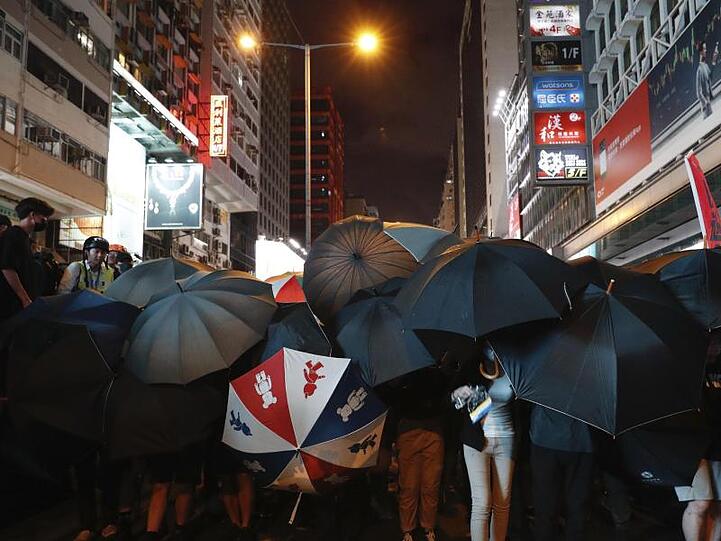 Demonstranten verbergen ihre Gesichter hinter Regenschirmen.
