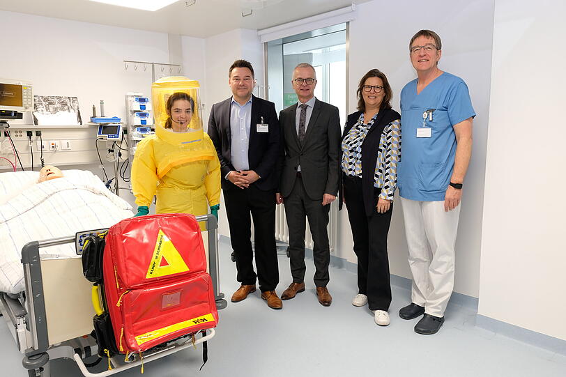 Bei der Wiederer&ouml;ffnung der Sonderisolierstation, v.l.n.r.: Im Schutzanzug eine Mitarbeitende des TUM Klinikums, die k&uuml;rzlich f&uuml;r die Sonderisolierstation geschult wurde. Daneben Dr. Tim Guderjahn (Kaufm&auml;nnischer Gesch&auml;ftsf&uuml;hrer, M&uuml;nchen Klinik), Dr. Rainer Hutka (Amtschef, Bayerisches Staatsministerium f&uuml;r Gesundheit, Pflege und Pr&auml;vention), Dr. Susanne Herrmann (Stellv. Gesundheitsreferentin, Landeshauptstadt M&uuml;nchen) und Dr. Wolfgang Guggemos (Leitender Oberarzt, Infektiologie der M&uuml;nchen Klinik Schwabing).