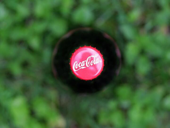 Der Deckel einer Coca Cola Flasche, die auf einer Wiese steht, ist zu sehen. Foto: Karl-Josef Hildenbrand/Archiv