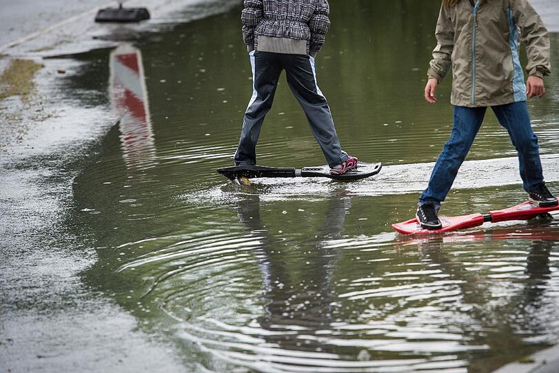 Zwei Kinder versuchen mit Streetboards durch die Fluten in Höchstadt an der Aisch.