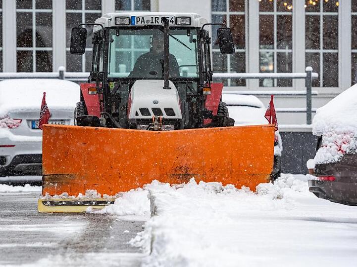 Mit einem Traktor wird Neuschnee von einem Parkplatz geräumt. Foto: Armin Weigel/dpa