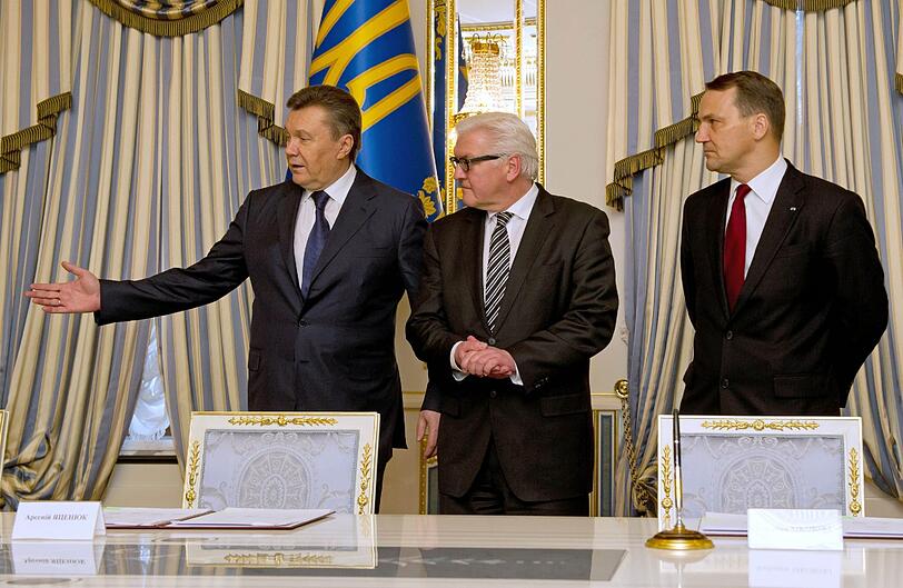 Der ukrainische Staatspräsident Viktor Janukowitsch (links),  Bundesaußenminister Frank-Walter Steinmeier (SPD) und der polnische Außenminister Radoslaw Sikorski stehen an einem Tisch im Präsidentenpalast in Kiew, auf dem Unterschriftenmappen bereit liegen.