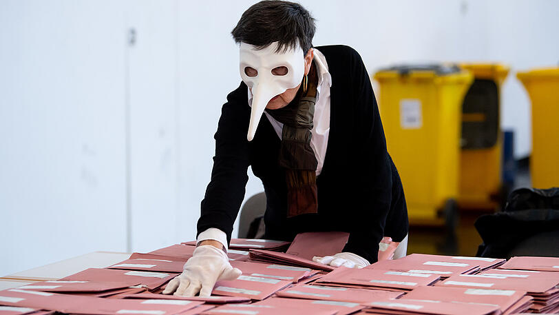 Makaberer Humor: Eine Wahlhelferin in München mit Handschuhen und Pestmaske. Solche Schnabelmasken wurden im 17. Jahrhundert von Ärzten getragen, die Pest-Patienten behandelten. Im Schnabel klemmte ein mit Essenzen getränkter Schwamm, da man damals davon ausging, dass die Pest über schlechte Luft, den sogenannten "Pesthauch" übertragen wurde.