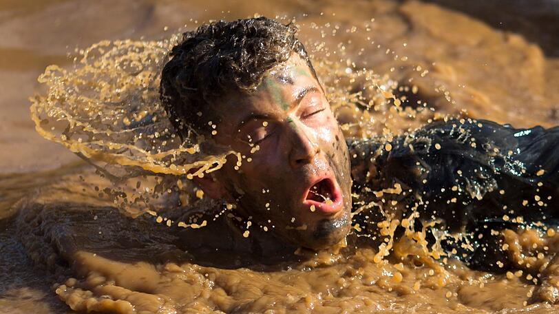 Ein Mann schwimmt durch Schlamm beim Mud Run, einem 10 km Hindernislauf.
