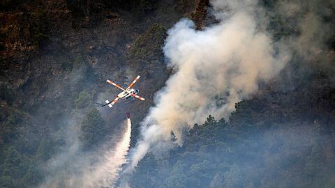 Ein Hubschrauber wirft Wasser auf die Flammen, während sich das Feuer durch den Wald in Richtung der Stadt Pinolere ausbreitet.