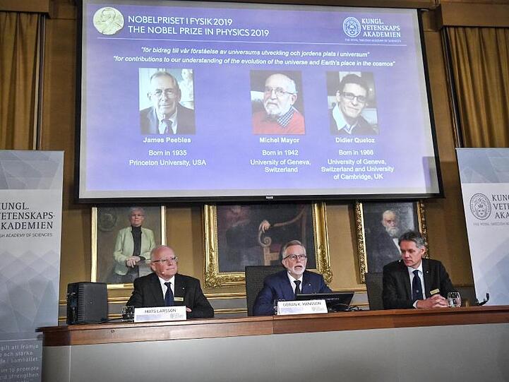 Der Nobelpreis für Physik geht in diesem Jahr an James Peebles (l-r auf der Leinwand), Michel Mayor und Didier Queloz.