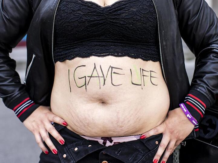 Eine Frau zeigt ihren Bauch mit der Aufschrift "I gave life" ("Ich habe Leben gegeben").