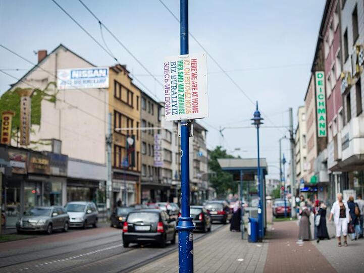 Ein Schild "Hier sind wir zuhause" in verschiedenen Sprachen hängt in Duisburg auf der Straße.