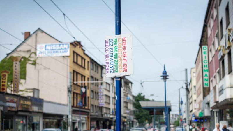 Ein Schild "Hier sind wir zuhause" in verschiedenen Sprachen hängt in Duisburg auf der Straße. Ein Schild "Hier sind wir zuhause" in verschiedenen Sprachen hängt in Duisburg auf der Straße.