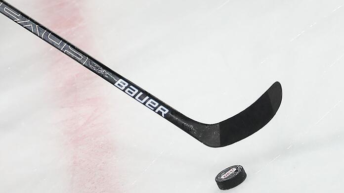 Ein Puck liegt vor einem Eishockey-Schläger auf dem Eis.