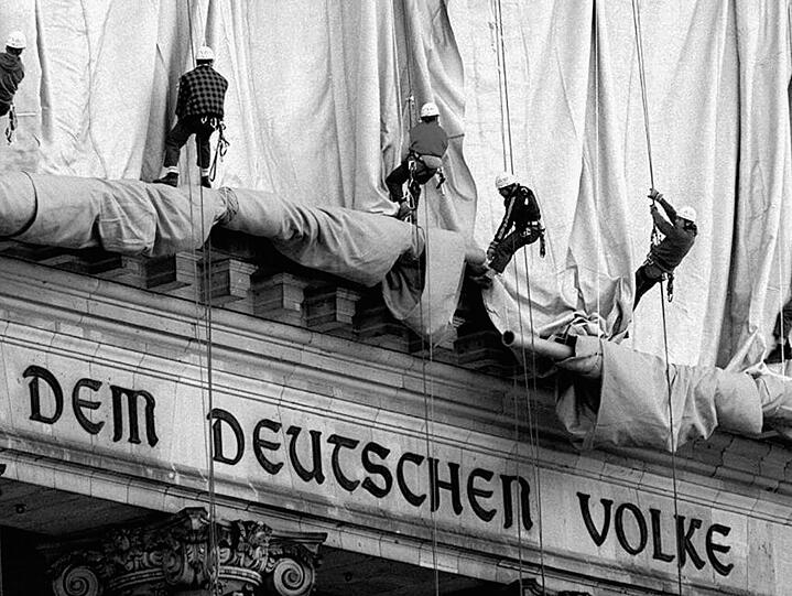 Eine lange Reihe von Gewerbekletterern rollt am frühen Montag morgen die Verhüllungsplanen für den Berliner Reichstag vom Giebel des Bauwerks.