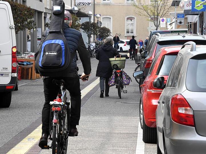 In Karlsruhe fahren Fahrradfahrer an Autos vorbei, die auf einem Parkstreifen stehen.