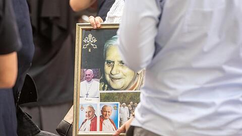 Eine Frau wartet mit einem Bild von dem emeritierte Papst Benedikt XVI. vor dem Haus von Georg Ratzinger. Foto: Armin Weigel/dpa/Archivbild