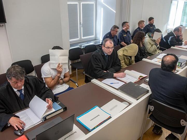 Die vier Angeklagten sitzen neben ihren Anwälten im Verhandlungssaal des Amberger Amtsgerichts.