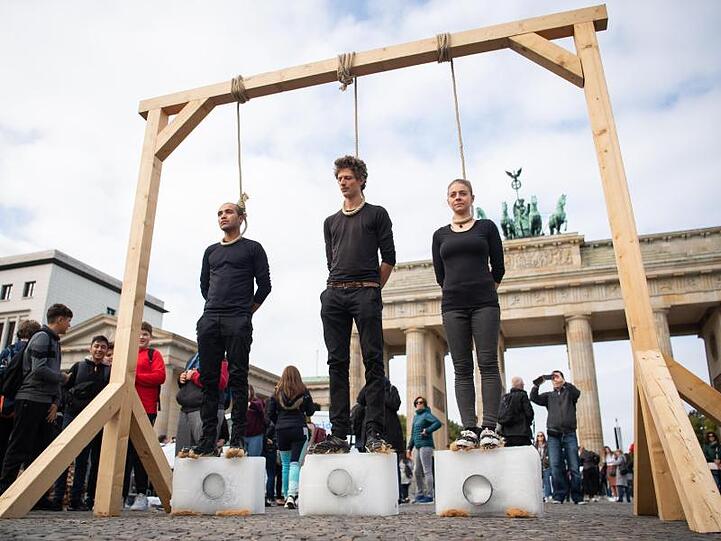 Vorm Brandenburger Tor: Drei Demonstranten stehen unter einem Galgen mit einem Seil um den Hals auf Eisblöcken.
